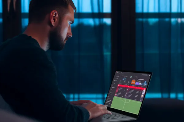 A man focused on his laptop with live stats in the background, highlighting the dedicated sports and gaming features of the 77ABC mobile app.