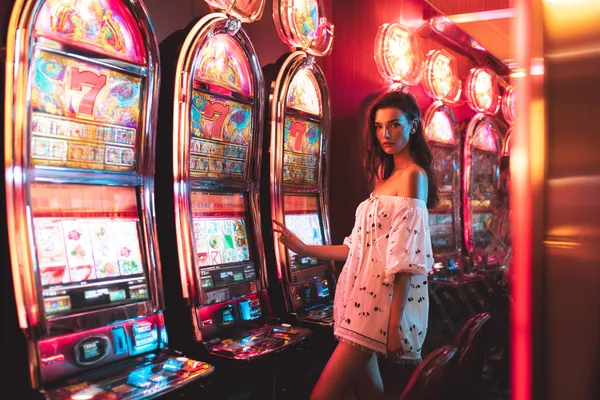 A stylish woman beside vibrant slot machines displaying glowing sevens, showcasing the variety of top slots at 77ABC.